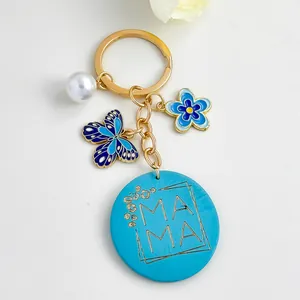 Detailopname van een blauwe houten sleutelhanger met MAMA gravure en vlinderbedel