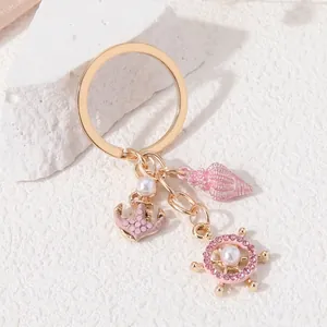 Detailed view of pink shell and ship wheel charms on gold ocean-themed keychain