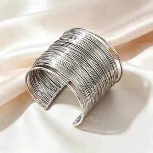Detail eines silbernen mehrlagigen Drahtarmreifs auf elegantem Seidenhintergrund