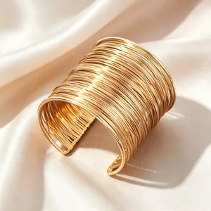 Nahaufnahme eines eleganten, goldfarbenen, mehrlagigen Drahtarmreifs auf Seidenstoff