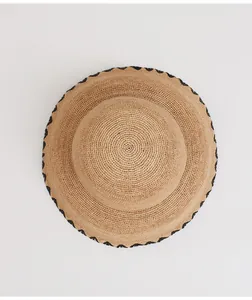 Close-up of a vintage raffia sun hat with black wavy trim on a white background.