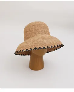 Handwoven raffia straw sun hat with decorative black zigzag edge on wooden stand