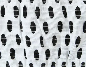 Nahaufnahme von weißem Gummizugstoff mit schwarzen ovalen Punkten und geraffter Textur.