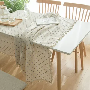 Detailed view of blue daisy floral pattern and tassel edges on a cream linen tablecloth.