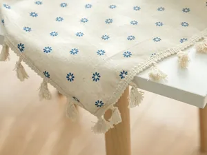 Close-up detail of the floral blue daisy print and cream tassel fringe on the tablecloth edge.