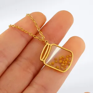 Macro detail view of gold-toned stainless steel mustard seed jar pendant held in hand