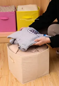 Detailed view of a beige foldable non-woven fabric storage box being filled with clothes.