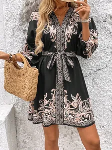 Dettaglio di un mini abito nero con stampa paisley, cintura in vita e scollatura a V
