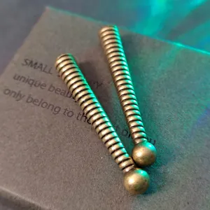 Primer plano de terminales de cordón en bronce con espiral y detalles de bola redonda