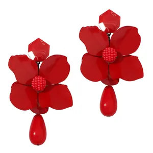 Macro view of red metal flower earrings with teardrop pendants on white background