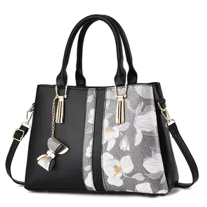 Bolso tote negro de cuero sintético con estampado floral y dije de lazo metálico