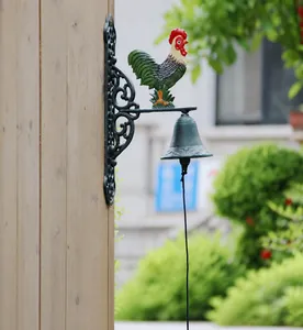 Detail view of vintage rooster iron doorbell on a wooden post in a garden setting.