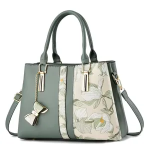 Primer plano del bordado floral y los herrajes dorados de este elegante bolso verde