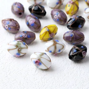 Primer plano de cuentas de vidrio lampwork hechas a mano con flores vintage y líneas doradas.