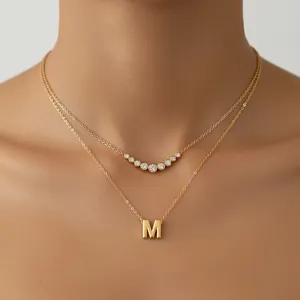 Primer plano de collar dorado a capas con colgante de letra M y detalle de cristal