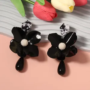 Close-up of black metal flower earrings with white pearl center and teardrop pendant.