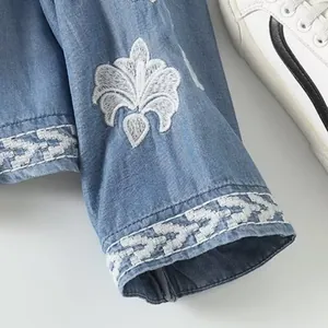 Detailed macro shot of white floral embroidery on a blue long-sleeved Tencel shirt