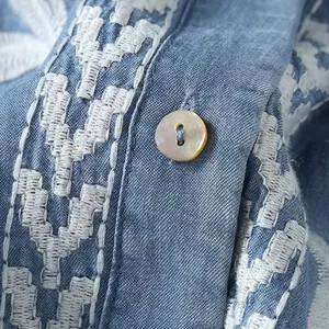 Macro view of intricate white ethnic embroidery and shell button on a blue Tencel shirt