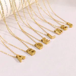 Detalle de collares de acero inoxidable dorados con iniciales sobre fondo blanco.