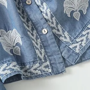 Close-up view of delicate white floral embroidery and shell buttons on a light blue tencel shirt.
