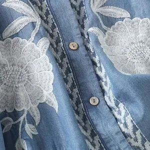 Close-up detail of white floral embroidery on a blue tencel shirt with buttons