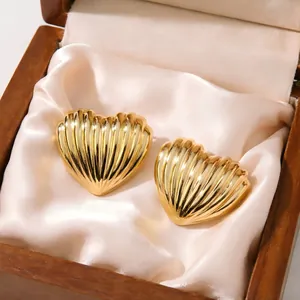 Close-up detail of vintage style gold ribbed heart stud earrings displayed on cream silk