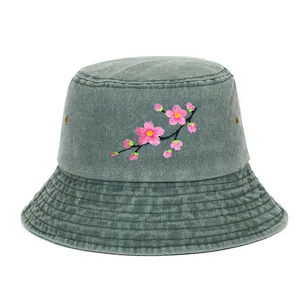 Close-up front view of a washed green bucket hat with pink cherry blossom embroidery
