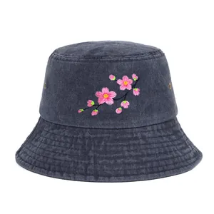Detailed macro view of delicate pink cherry blossom embroidery on dark denim bucket hat