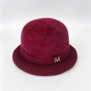 Detailed view of burgundy rabbit fur knit hat with silver metal M logo ornament.