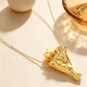 Dettaglio di una collana con ciondolo a bouquet dorato e piccole piante essiccate.