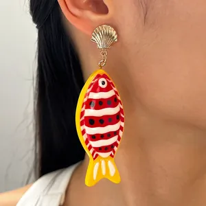 Détail d'une boucle d'oreille poisson tropical coloré avec clou en coquillage doré.