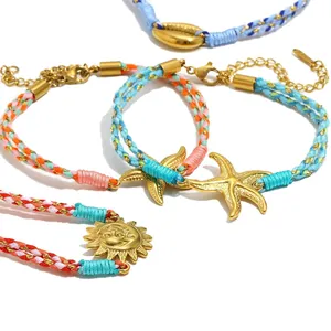 Nahaufnahme von vergoldeten Seestern- und Sonnenanhängern an bunten geflochtenen Armbändern.