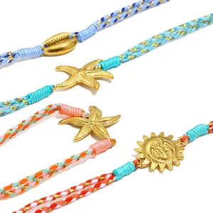 Detailansicht von 18K vergoldeten Seestern- und Sonnenanhängern an geflochtenen Armbändern.