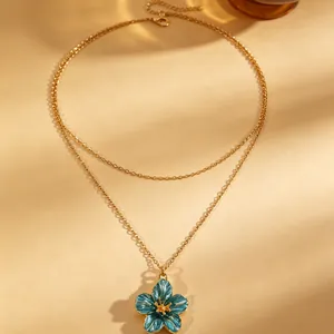 Detailed macro shot of a double-layered gold necklace featuring a blue enamel flower pendant