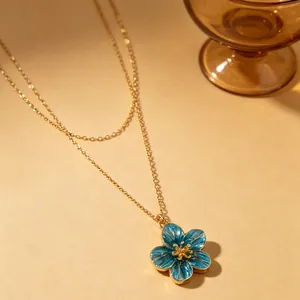 Close-up of a blue enamel flower pendant on a double-layer gold necklace chain