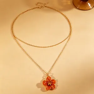 Close-up of double-layered gold necklace with orange enamel flower pendant