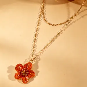 Detailed macro close-up of an orange enamel flower pendant on a dainty gold chain.
