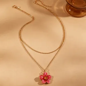 Detail shot of a layered gold necklace featuring a vibrant pink flower enamel pendant.