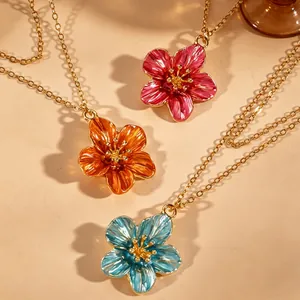 Close-up view of elegant enamel flower necklaces in pink, orange and blue with gold chains