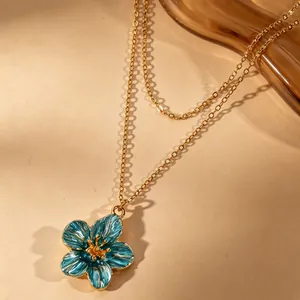 Detailed view of a sweet blue enamel flower pendant on a delicate gold chain necklace