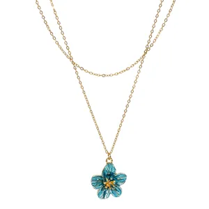 Macro detail of blue enamel flower pendant on delicate double-layered gold-tone chain