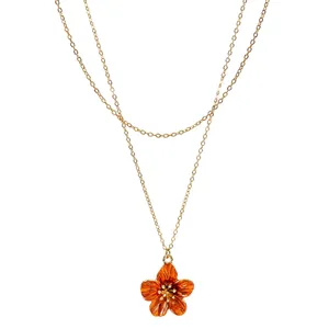 Detailed close-up of orange enamel flower pendant on elegant layered gold chain