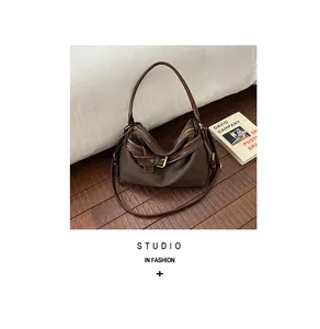 Brown canvas shoulder bag with leather trim and buckle detail in a cozy home setting