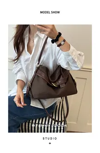 Close-up of a stylish brown canvas crossbody bag worn by a model in a white shirt.