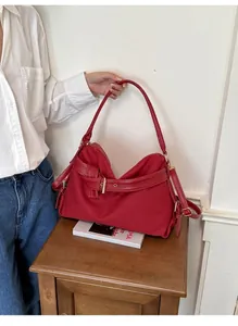 Close-up of a red minimalist canvas shoulder bag held by a model in a casual setting.
