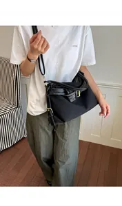 Detail view of a stylish black minimalist crossbody bag with buckle accent on model.