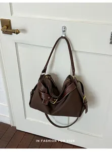 Stylish brown canvas shoulder bag with leather trim hanging on a vintage white door