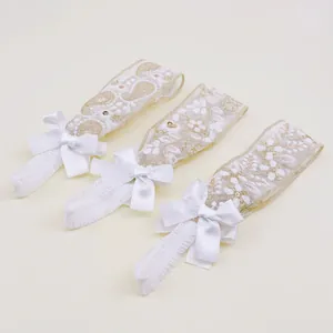 Close-up of three white lace baby headbands with floral embroidery and satin bows.