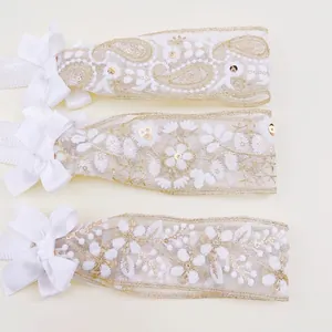 Detailed view of three white lace baby headbands with elegant gold embroidery