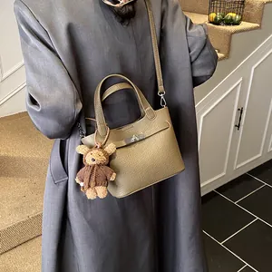 Elegant khaki leather bucket bag featuring a silver lock and cute brown teddy bear charm